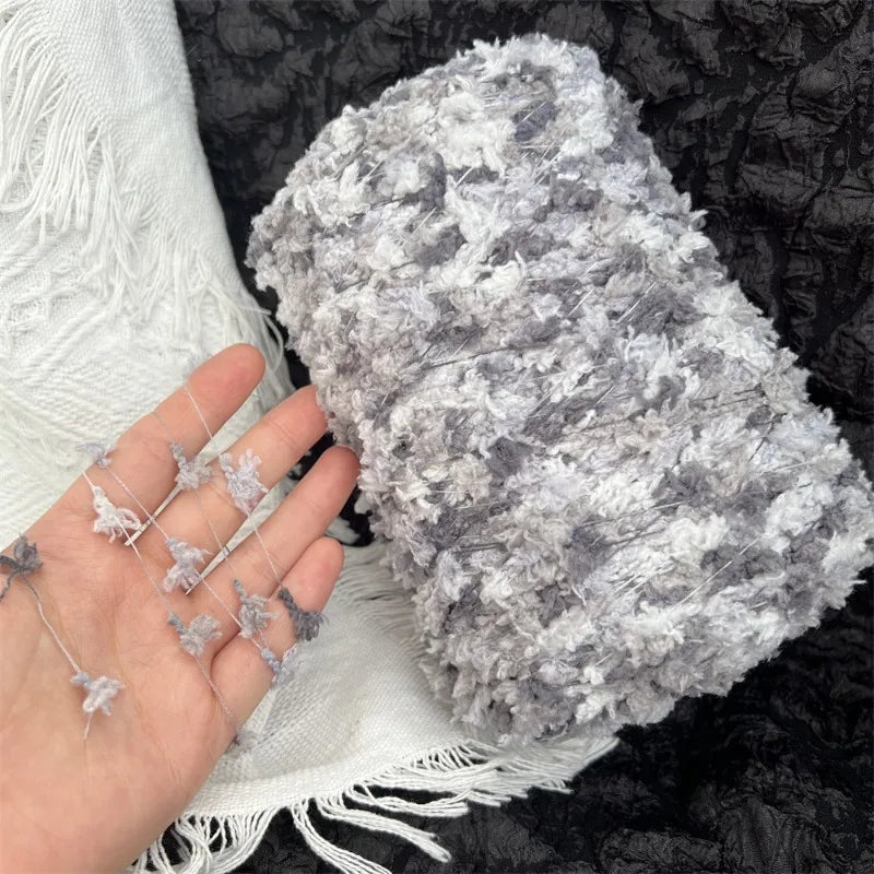 A hand holding a skein of gray and white variegated cotton blend yarn for knitting and crochet