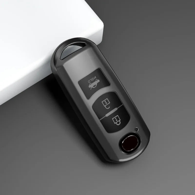 A close-up view of a black TPU car key cover with various buttons and a lens, resting on a gray surface.