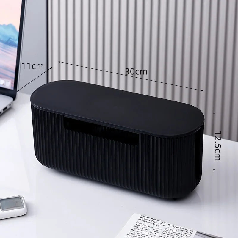 A black cable management box with ribbed sides is shown on a white desk surface.
