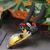 A pair of black and red precision pruning shears with a gold-colored blade resting on a dark wooden surface surrounded by gre