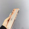 A hand holds an iPhone in a clear glow-in-the-dark neon orange case against a light gray background.