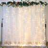 Three sheer white tulle curtains with warm fairy lights draped for an event backdrop.