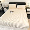 A thick, cream-colored knit fitted bed sheet is displayed on a bed with a black headboard and white bedding.