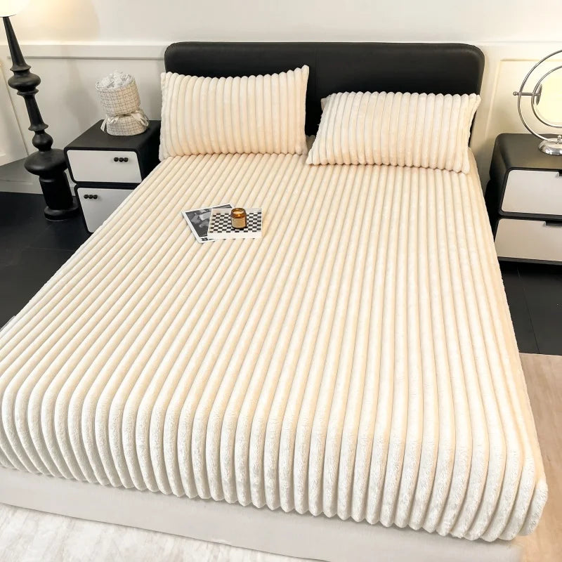 A thick, cream-colored knit fitted bed sheet is displayed on a bed with a black headboard and white bedding.