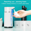 A hand is demonstrating a touchless soap dispenser, showing the foam being dispensed from the device.
