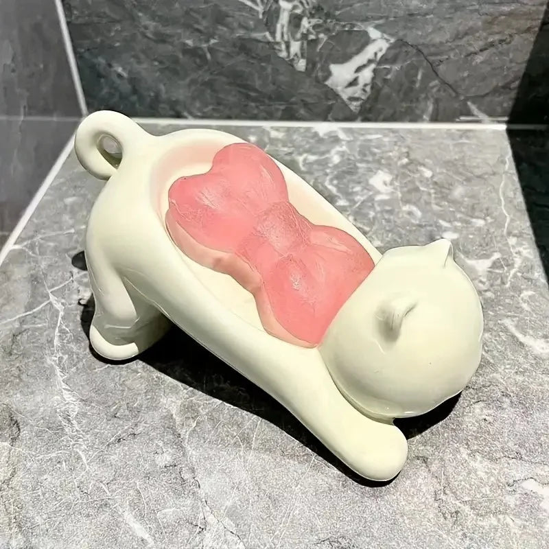 A white cat-shaped soap dish with a pink bow design resting on a gray marble surface.