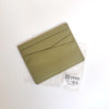 A slim card holder wallet made of olive green genuine leather, packaged in a clear plastic sleeve.