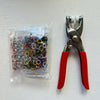 Un par de pinzas plateadas y rojas con cinco mordazas para sujetar, descansando sobre una superficie blanca junto a una bolsa