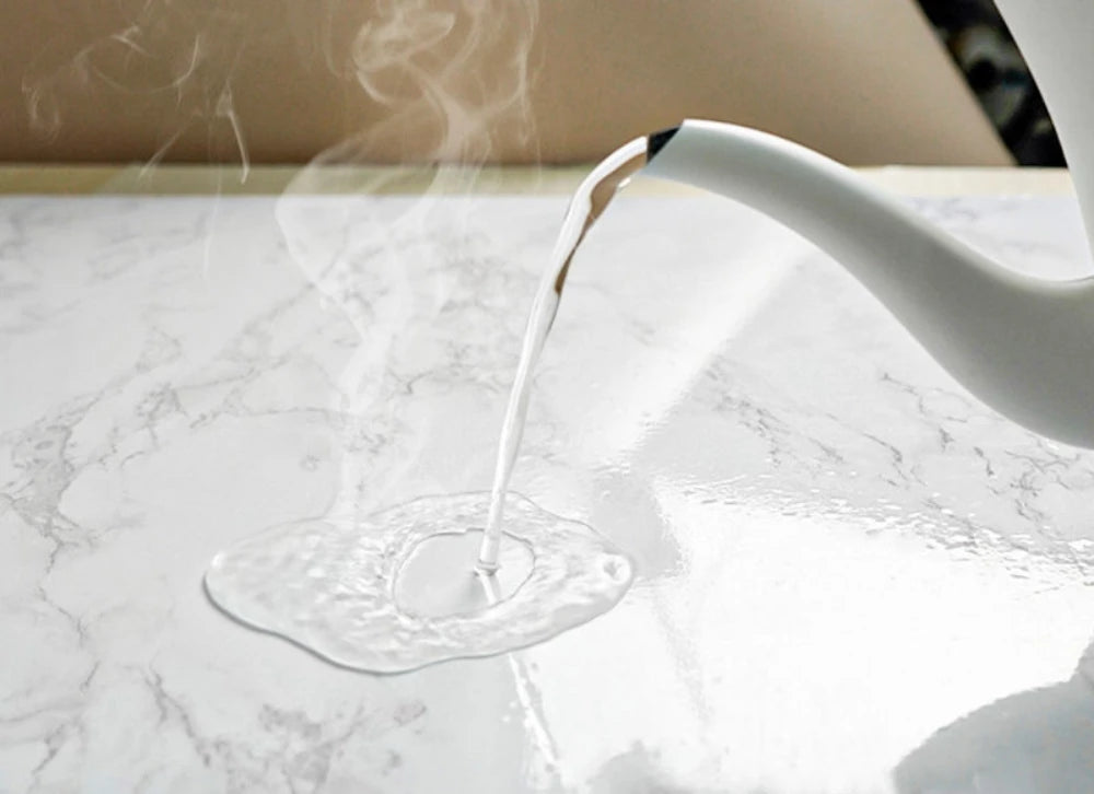 A white liquid is being poured from a white bottle onto a marble surface, creating a visible steam or mist.