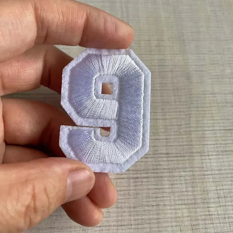 A hand holds a white iron-on 3D number patch shaped like the numeral nine.