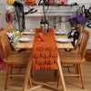 An autumn pumpkin and ghost themed table runner set on a wooden dining table with seasonal decorations.