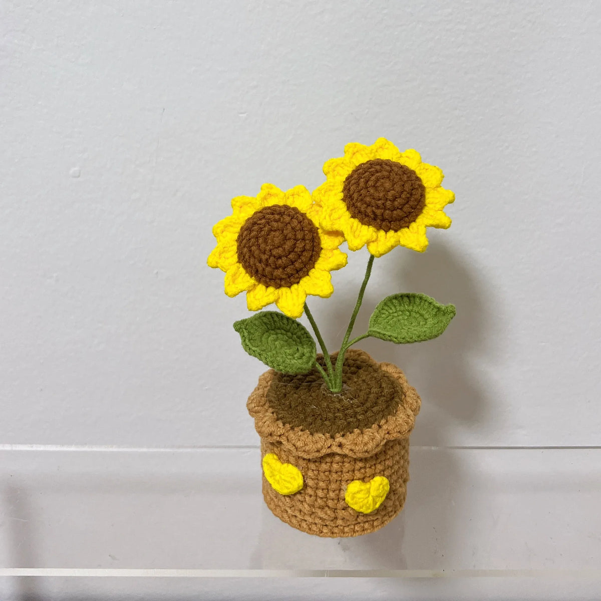 Handcrafted crochet sunflower with green leaves growing in a brown crocheted pot