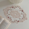 Elegant oval lace embroidered placemat with pink floral embroidery on a white background