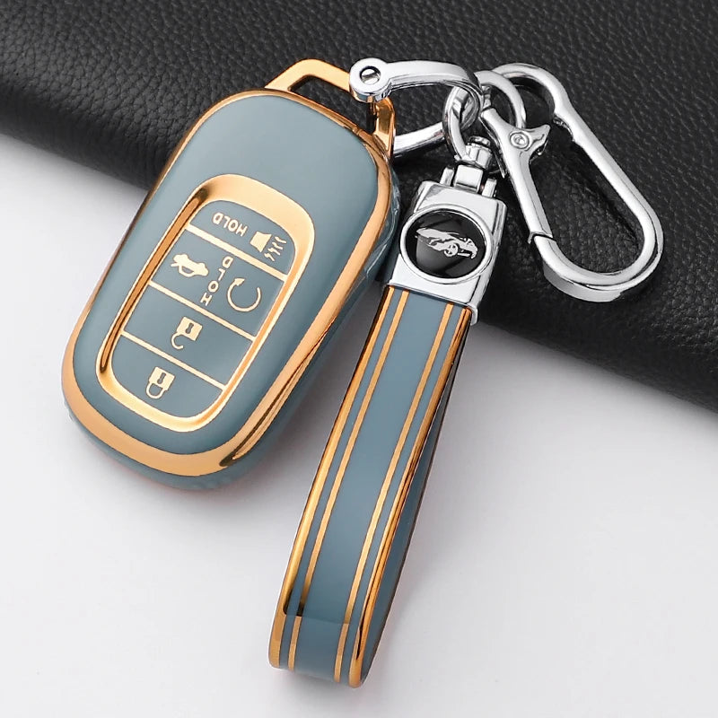 A gold and gray Honda key fob cover with a protective case and attached keyring, resting on a black surface.