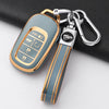 A gold and gray Honda key fob cover with a protective case and attached keychain on a black surface.