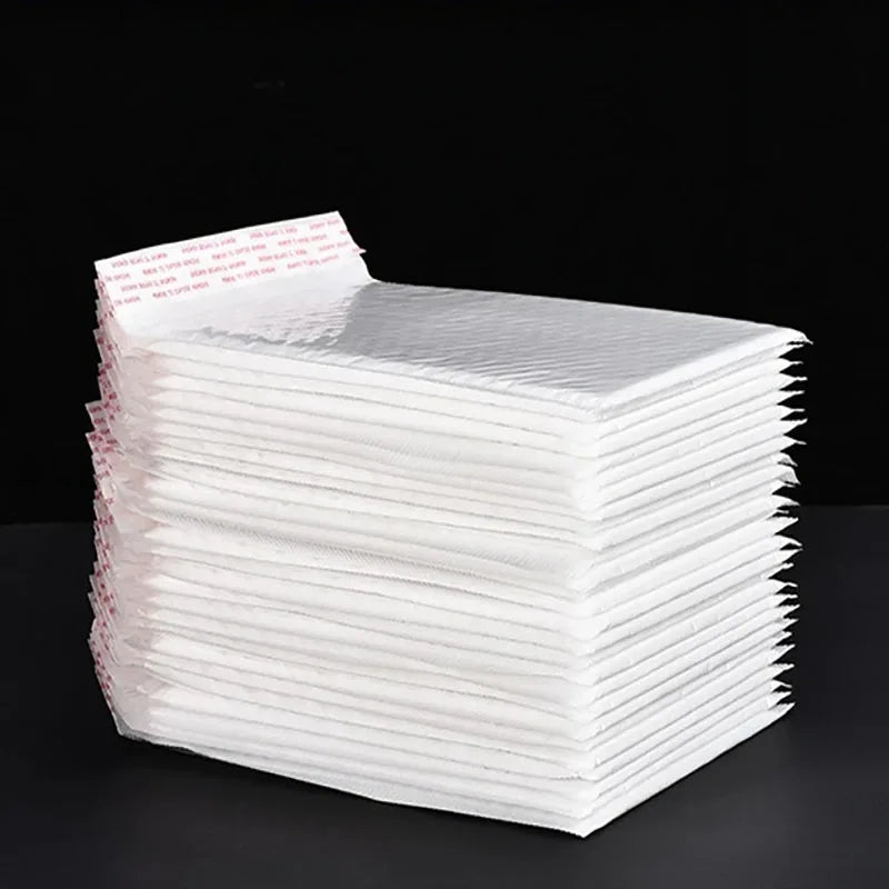 A stack of white padded bubble mailers with self-seal closures is displayed on a dark surface.