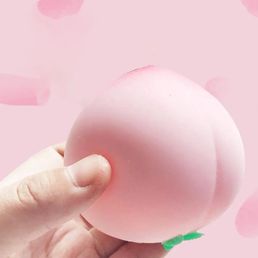 Une main serre un jouet stress-ball pêche rose contre un fond rose pâle.