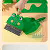A hand is using a green cartoon broom and dustpan set for cleaning on a light-colored surface.