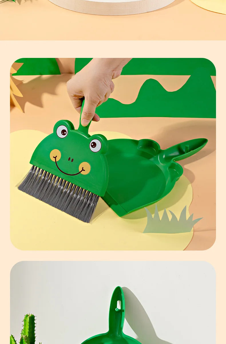 A hand is using a green cartoon broom and dustpan set for cleaning on a light-colored surface.