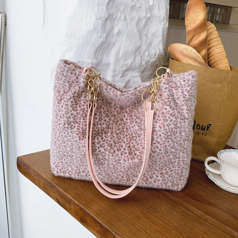 Sac en toile canvas à imprimé léopard rose avec quincaillerie dorée posé sur une surface en bois.