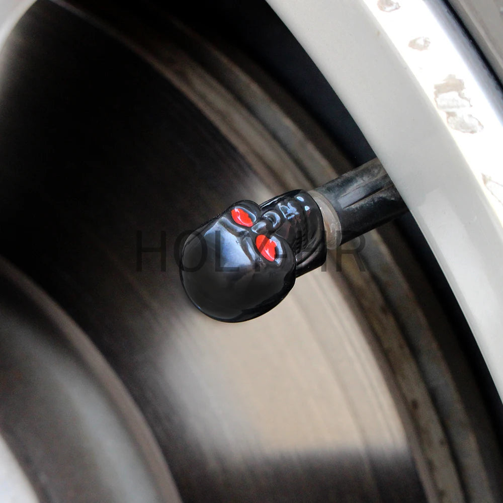 Close-up view of four black skull design tire valve stem caps on a tire rim.