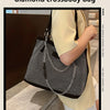 A woman holds a black diamond crossbody bag with a silver chain against a light yellow shirt.