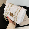 A white quilted bag with gold chain straps is held by a hand against a black background.