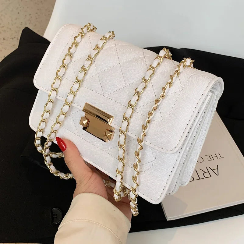 A white quilted bag with gold chain straps is held by a hand against a black background.