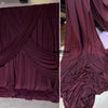 A close-up of elegant burgundy stretch jersey fabric draped in folds for decor and backdrops.