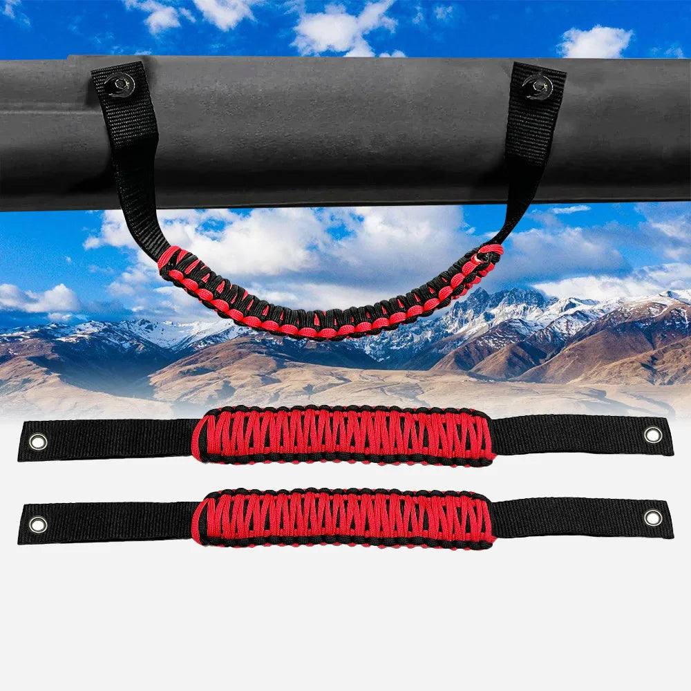 Black paracord grab handles with red accents shown attached to a vehicle bar against a scenic mountain backdrop.