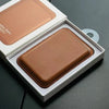 A brown leather wallet case with MagSafe compatibility is displayed inside its white box.