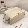 A beige waterproof PU leather cosmetic bag resting on a white surface next to a ceramic vessel.