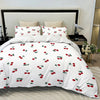 White duvet cover set with a red cherry print and matching pillowcases displayed on a bed.