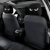 A pair of black car headrest covers with slanted eyes are shown inside a vehicle cabin.