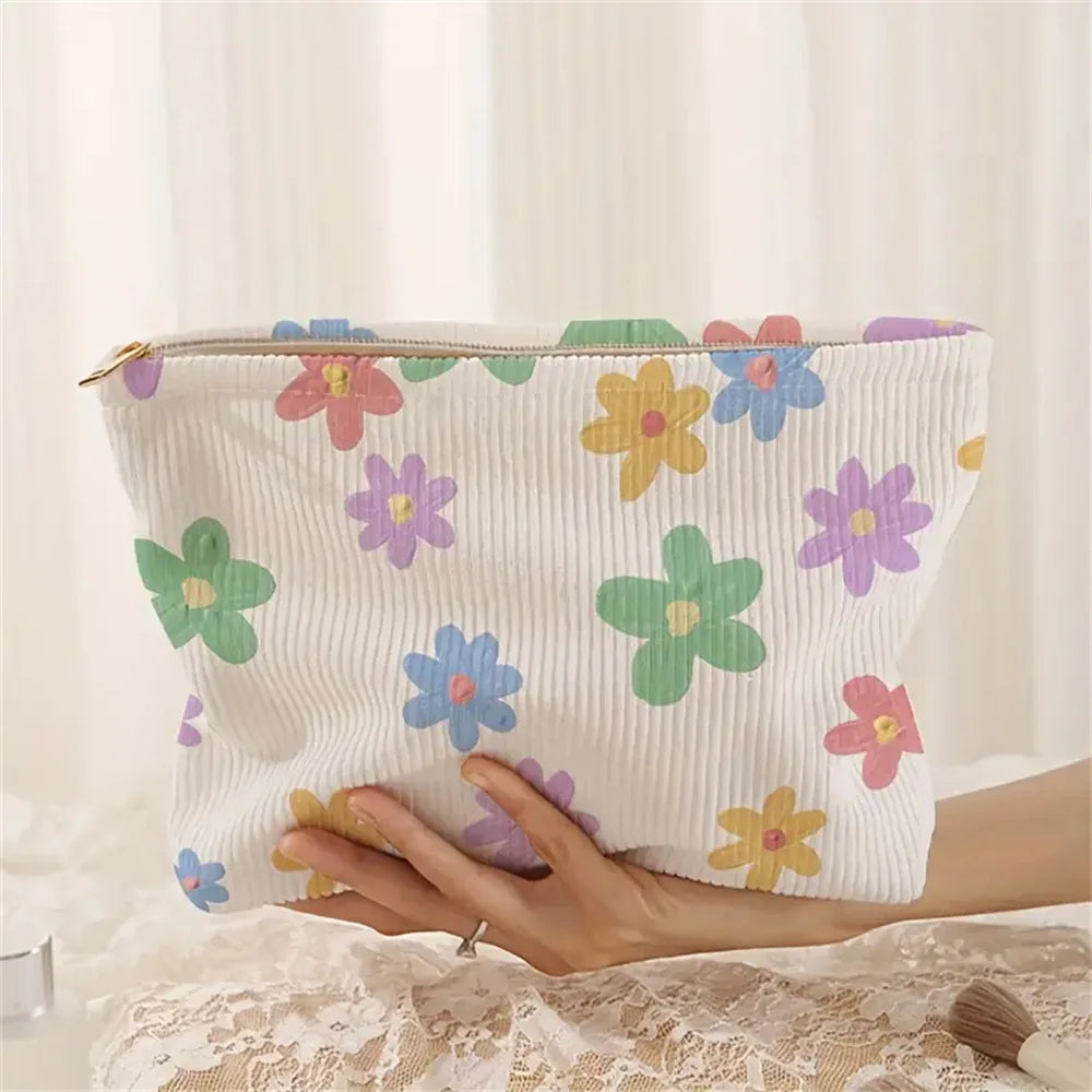 A white floral corduroy makeup bag with a pink zipper is held by a hand on a lace surface.