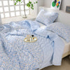 Light blue floral quilted blanket and pillow set displayed on a white bed.