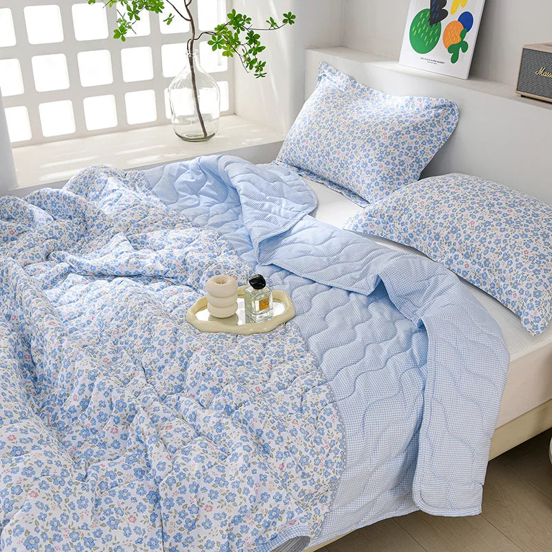 Light blue floral quilted blanket and pillow set displayed on a white bed.