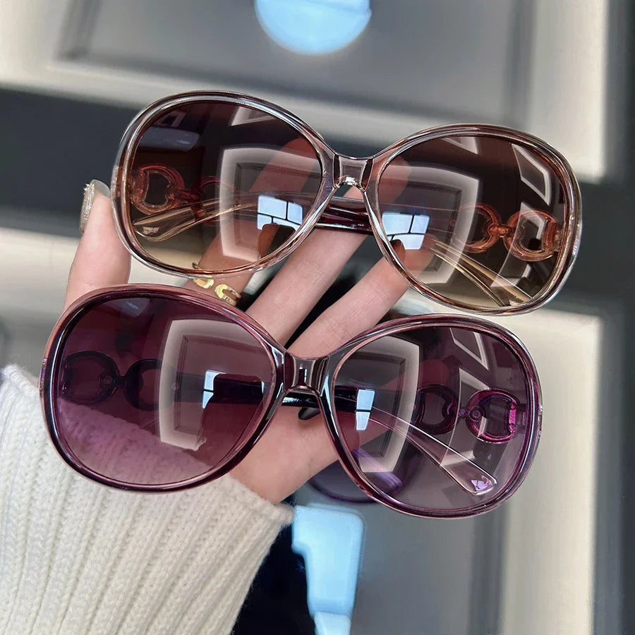 A hand holds a pair of square vintage sunglasses with tinted lenses and gold-toned frames.