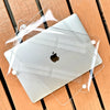 A clear protective case is placed over a silver MacBook, resting on a wooden surface.