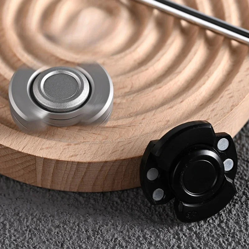 A silver stainless steel fidget spinner and slider resting on a light wooden surface.