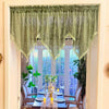 A sheer sage green lace curtain valance with fringe hangs over a window in a bright room.