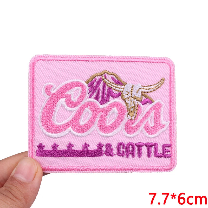 Pink embroidered patch with the word Cools and Cattle in pink and gold thread