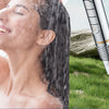 A woman is showering under a high-pressure filtered shower head, with water streaming down her hair and body.