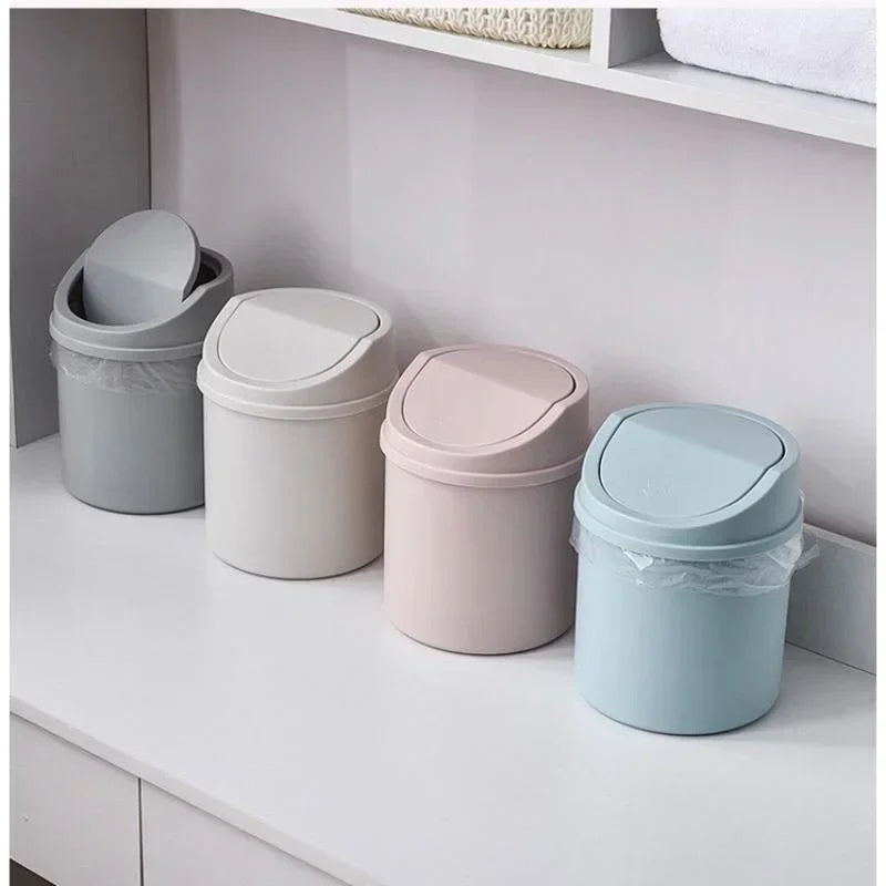A row of four compact covered desktop trash bins in various pastel colors, including gray, white, pink, and light blue.