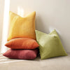 Three vertically ribbed corduroy throw pillows in shades of yellow, orange, and olive green