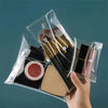 A hand holds a clear cosmetic bag containing makeup brushes and a lip product.