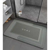 A rectangular gray bath mat with a non-slip rubber base is placed on a dark tiled floor inside a shower enclosure.
