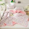 A pink and white quilted blanket is displayed on a bed, featuring a floral pattern.