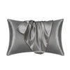 Funda de almohada de seda satinada gris suave y elegantemente drapeada.