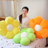 A collection of lifelike sunflower plush pillows in yellow, orange, and green are displayed on a white surface.